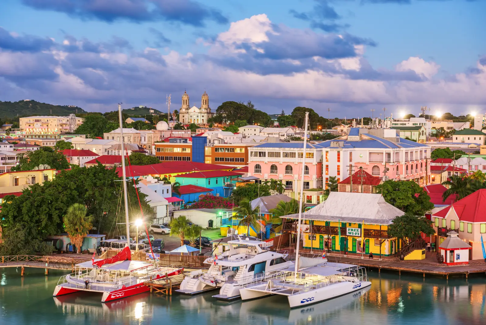 Waterfront view of St. John’s, Antigua at dusk with colorful buildings and boats along the quay.