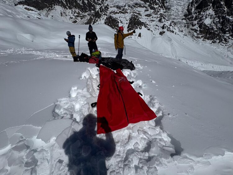 Four rescuers on a snowy surface where they have dug avalanche victims and covered them with a red blanket.