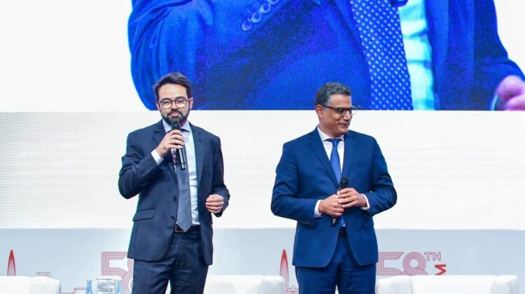 Yann Cabaret, CEO of SITA for Aircraft, and Maher Koubaa, executive VP, travel unit and managing director EMEA at Amadeus, on stage to announce the companies' partnership with AACO to improve transparency on air travel emissions. There is a white and blue screen behind them with company logos.