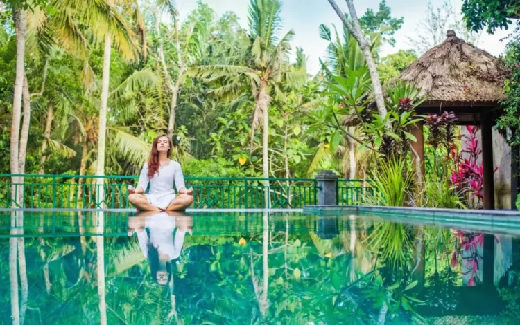 Woman meditating by a tropical pool at a wellness resort surrounded by lush greenery