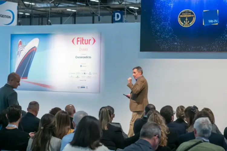 Conference speaker addresses an audience at FITUR Cruises in Madrid, with cruise branding visible on stage.