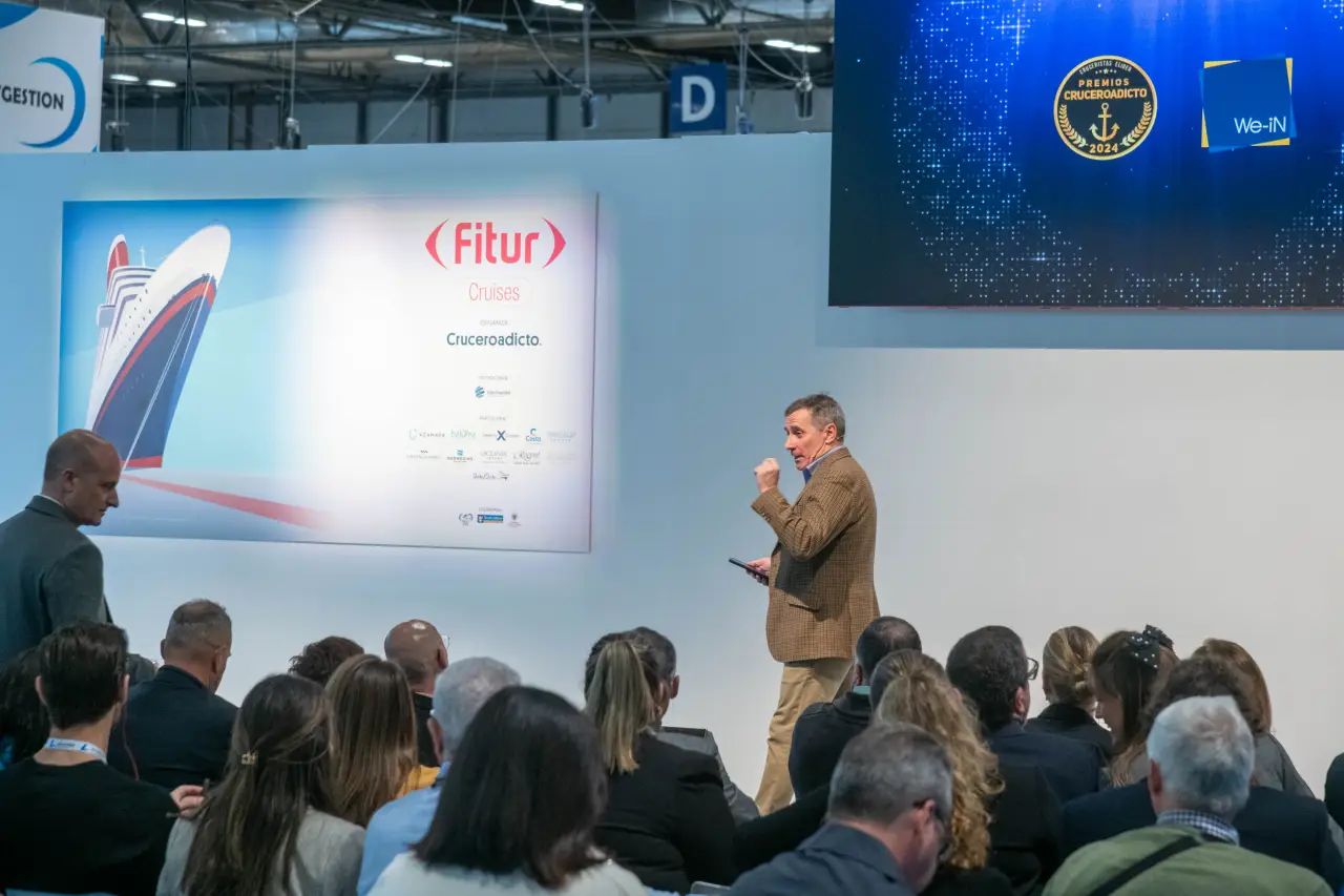 Conference speaker addresses an audience at FITUR Cruises in Madrid, with cruise branding visible on stage.
