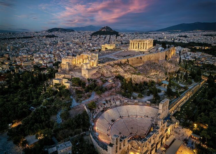Aerial view of illuminated, ancient ruins at the Acropolis of Athens, Greece, and Odeon of Herode theatre during dusk. Photo source: Visit Greece
