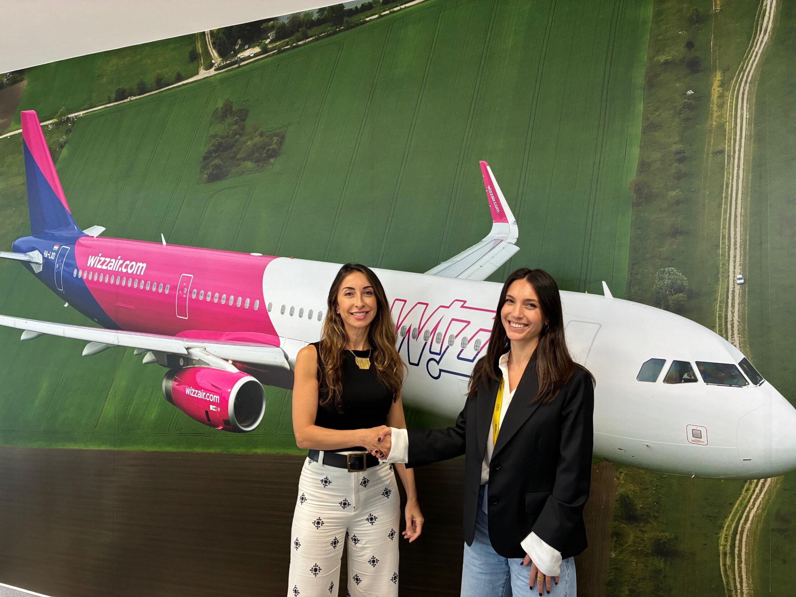 Silvia Mosquera and Alice Ferrari shake hands with an image of a Wizz Air aircraft behind them