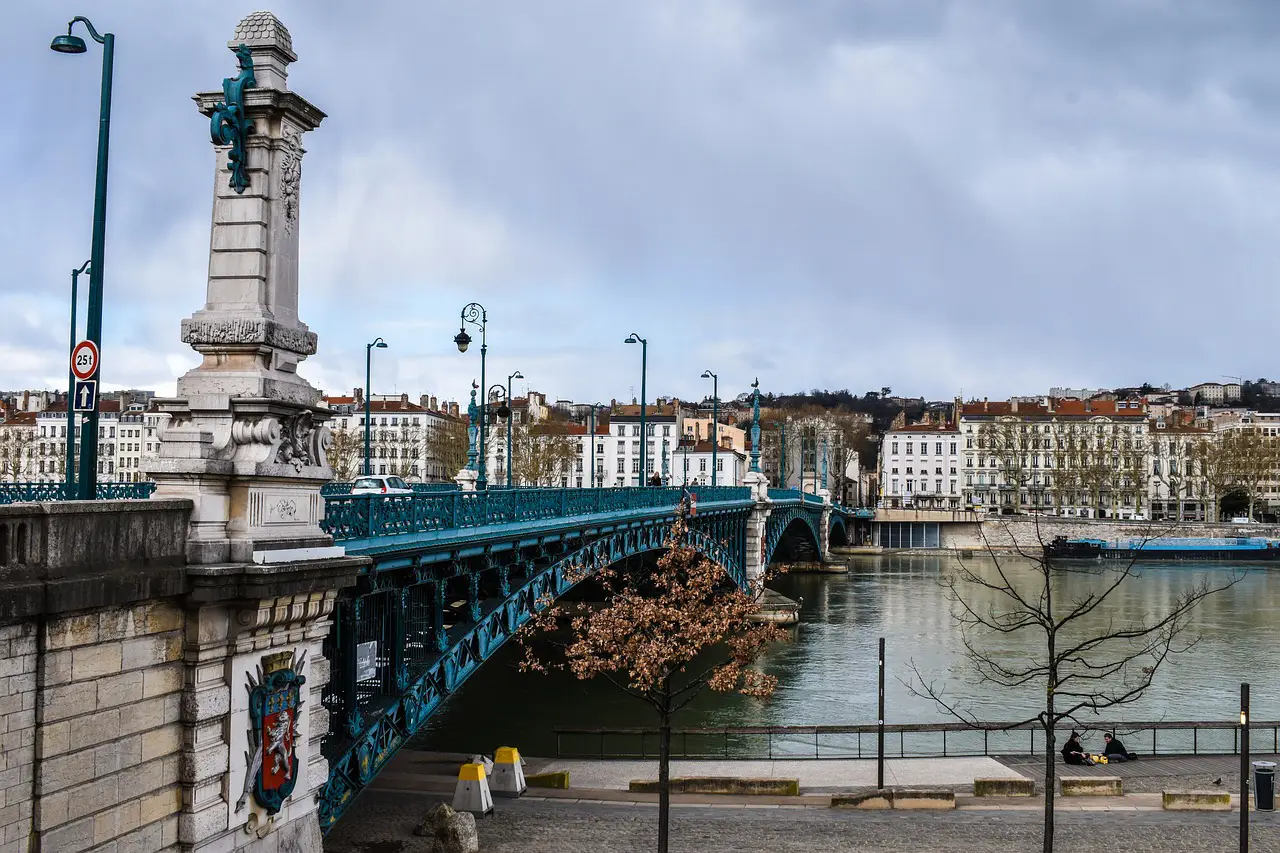 A historic bridge in Lyon, France, spanning the Rhône River with ornate lampposts and decorative sculptures, surrounded by classic European buildings.