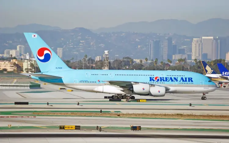 Korean Air Airbus A380 taxiing on a runway with a city skyline and mountains in the background.