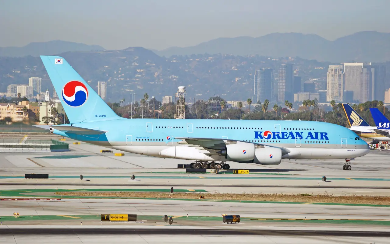 Korean Air Airbus A380 taxiing on a runway with a city skyline and mountains in the background.