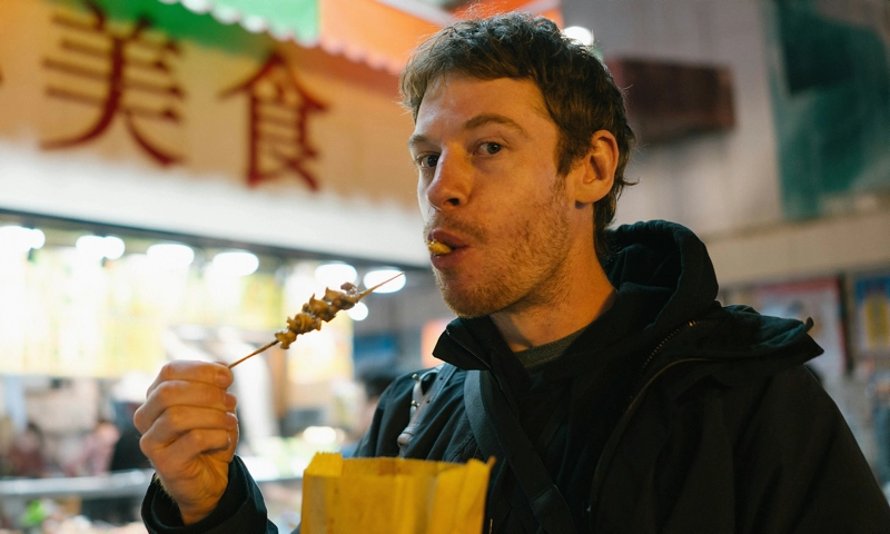 A man holding a bag of food and eating from a skewer