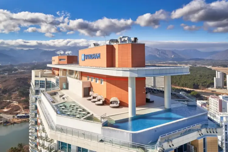 Rooftop view of Wyndham’s first managed hotel in South Korea, featuring an infinity pool, terrace seating, and mountain scenery under a blue sky.