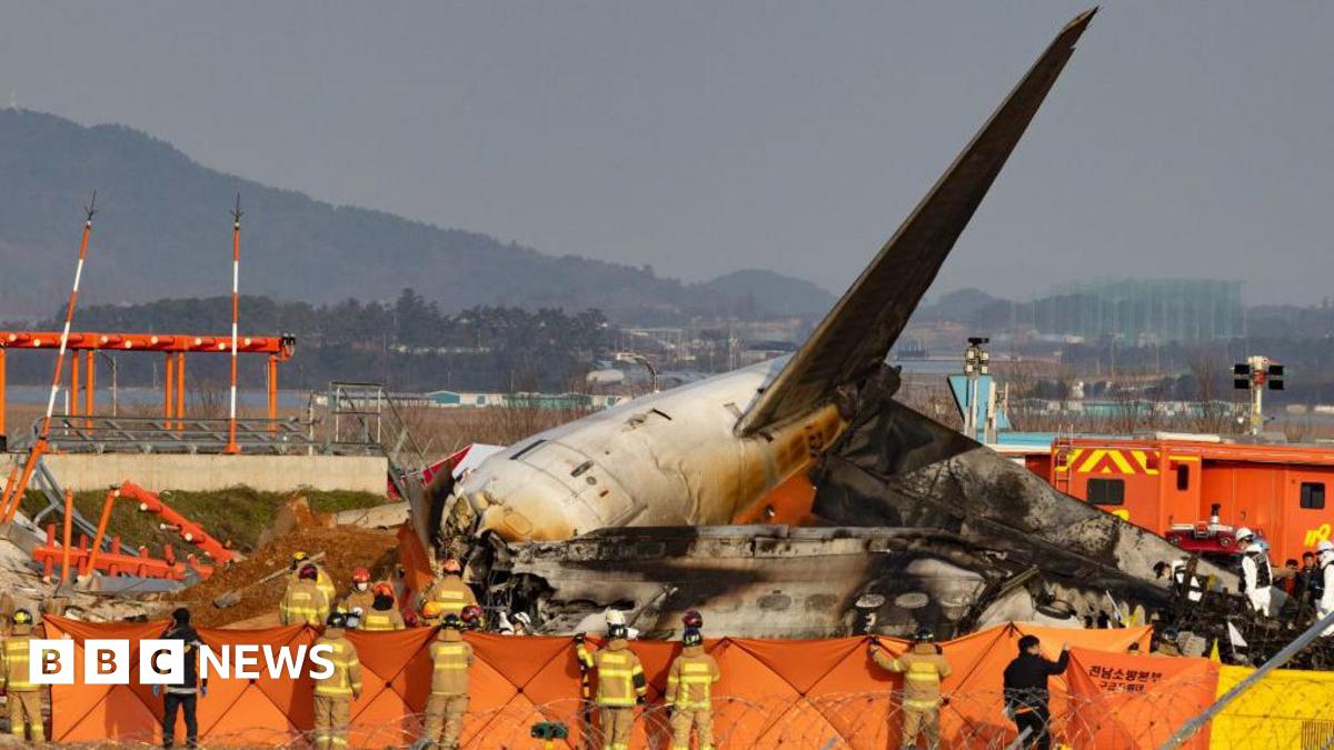 The charred tail of Jeju Air Flight 2216 surrounded by firefighters at the end of the runway in Muan Airport in south-west South Korea