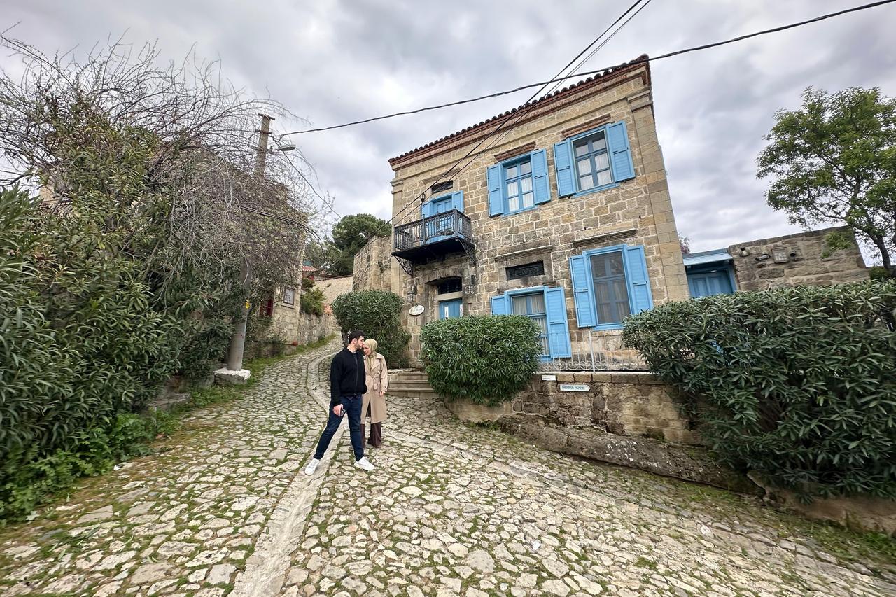 A view of a traditional stone house with blue shutters along a narrow street in Adatepe village, Canakkale, Türkiye. (AA Photo)