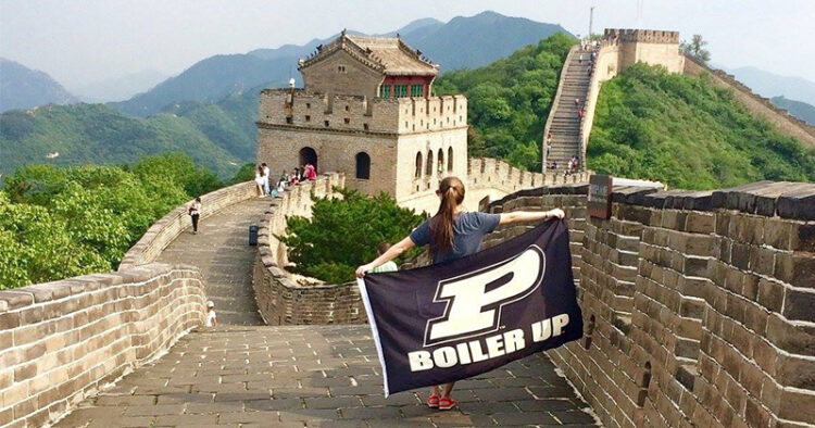 A student walks along the Great Wall of China holding a flag behind her that says "Boiler Up" with the Purdue logo.