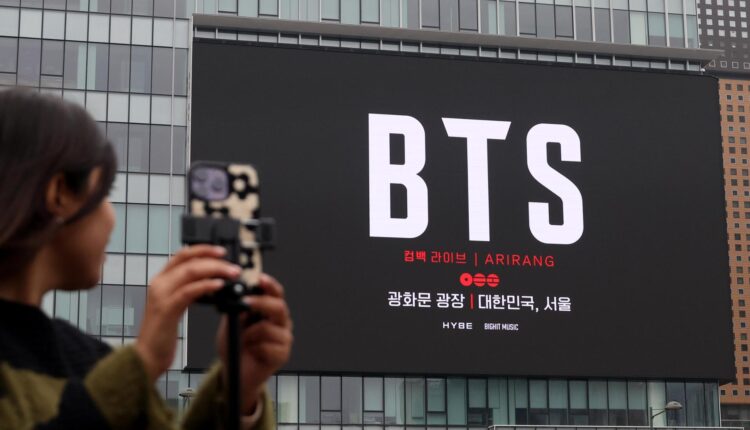 A woman looks at a screen promoting BTS