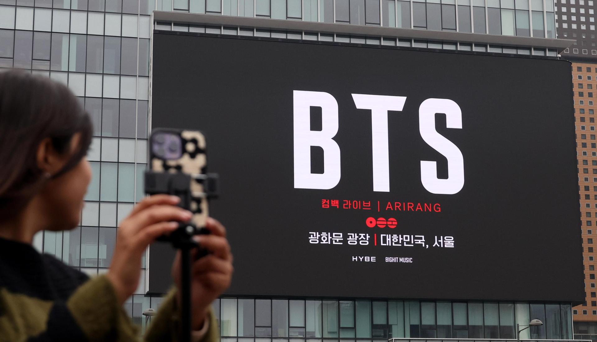 A woman looks at a screen promoting BTS