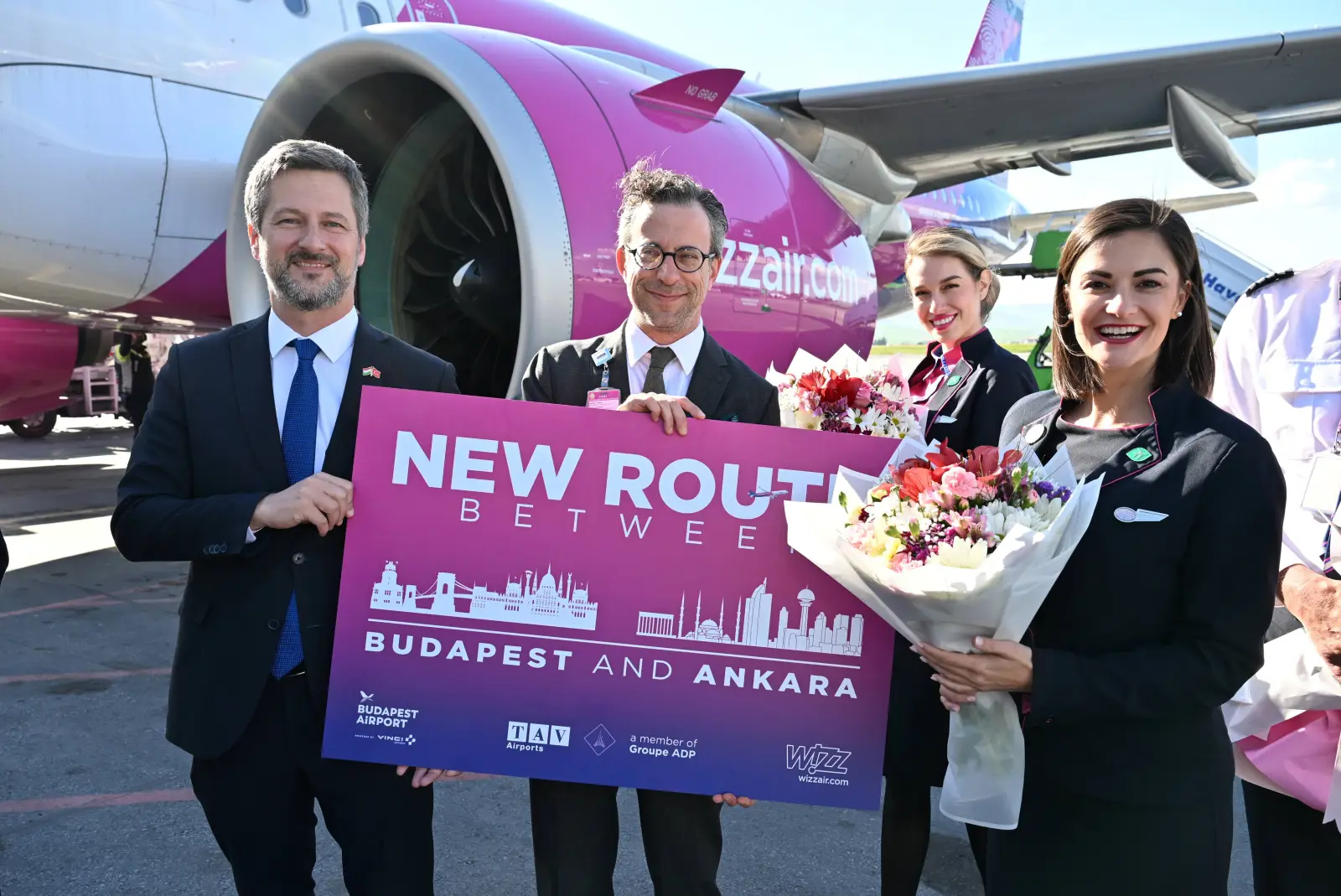 Officials and Wizz Air crew celebrate the launch of direct Budapest to Ankara flights beside a Wizz Air aircraft at Ankara Esenboğa Airport.