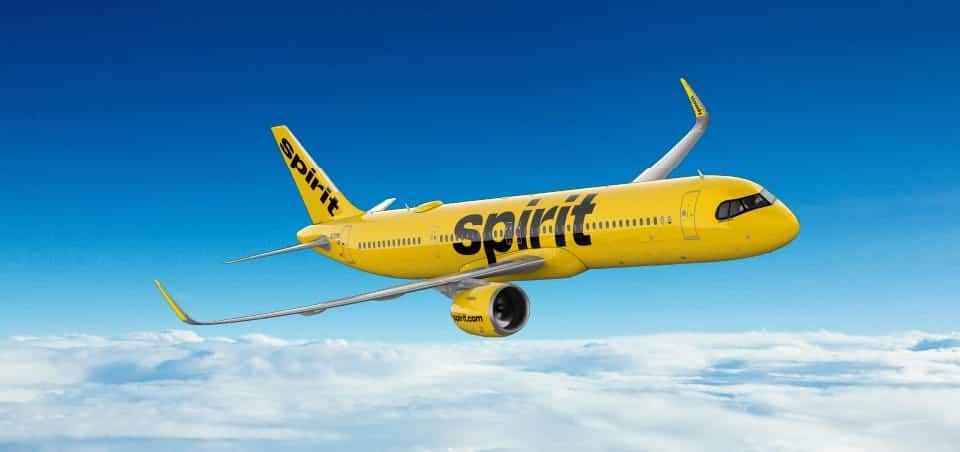 Spirit airlines plane in flight above clouds, disrupting travel plans.
